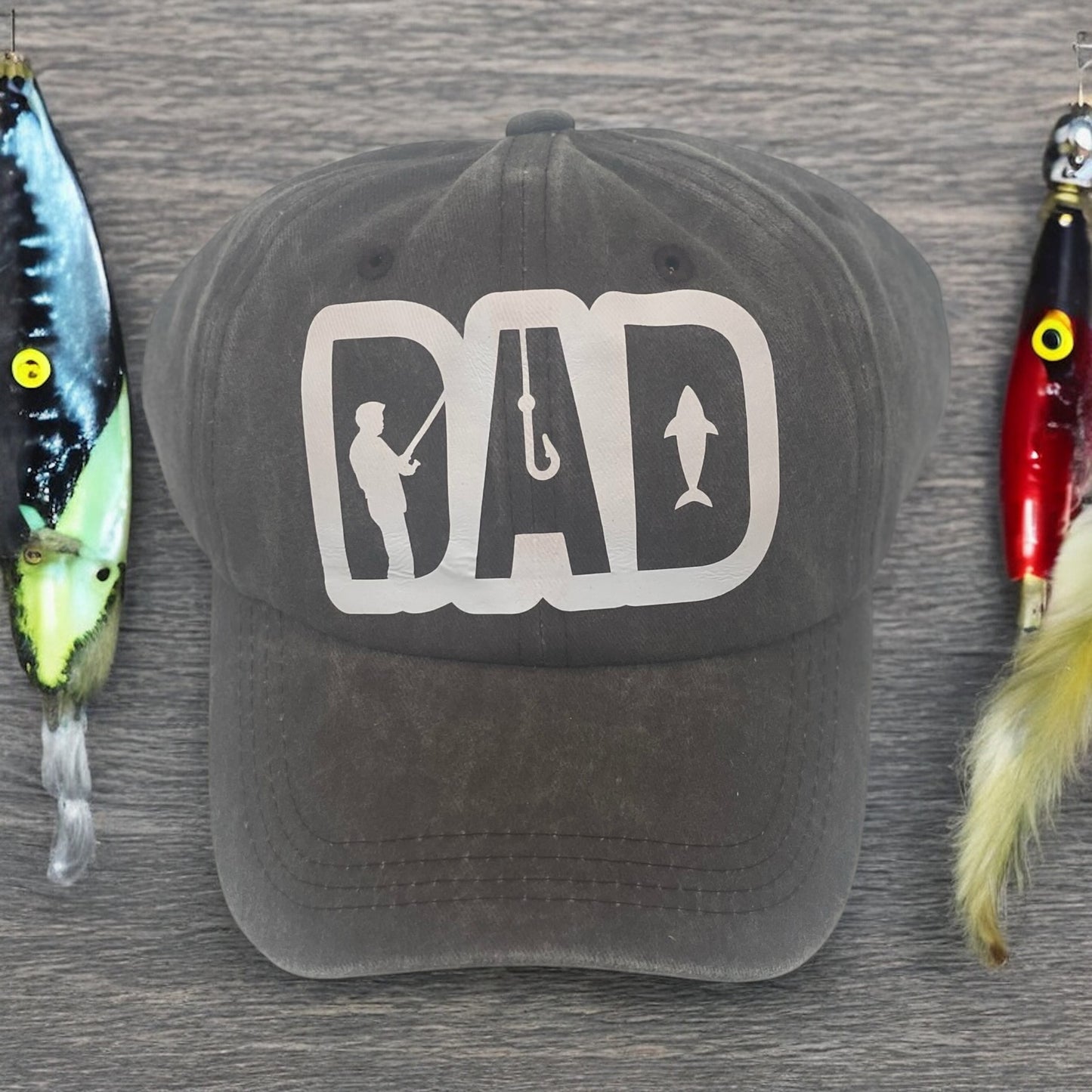 A brown baseball cap with a white 'DAD' logo featuring a silhouette of a person with a fishing rod.