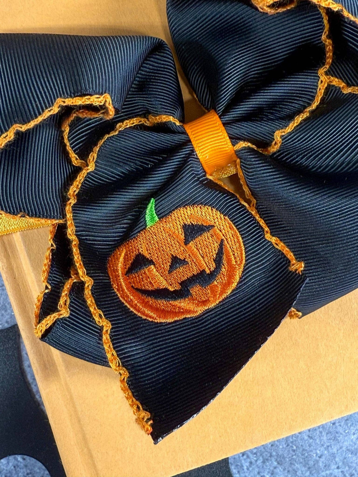 Seaside Custom Apparel & Gifts black hair bow with orange jack-o-lantern embroidery and decorative moonstitch edges.