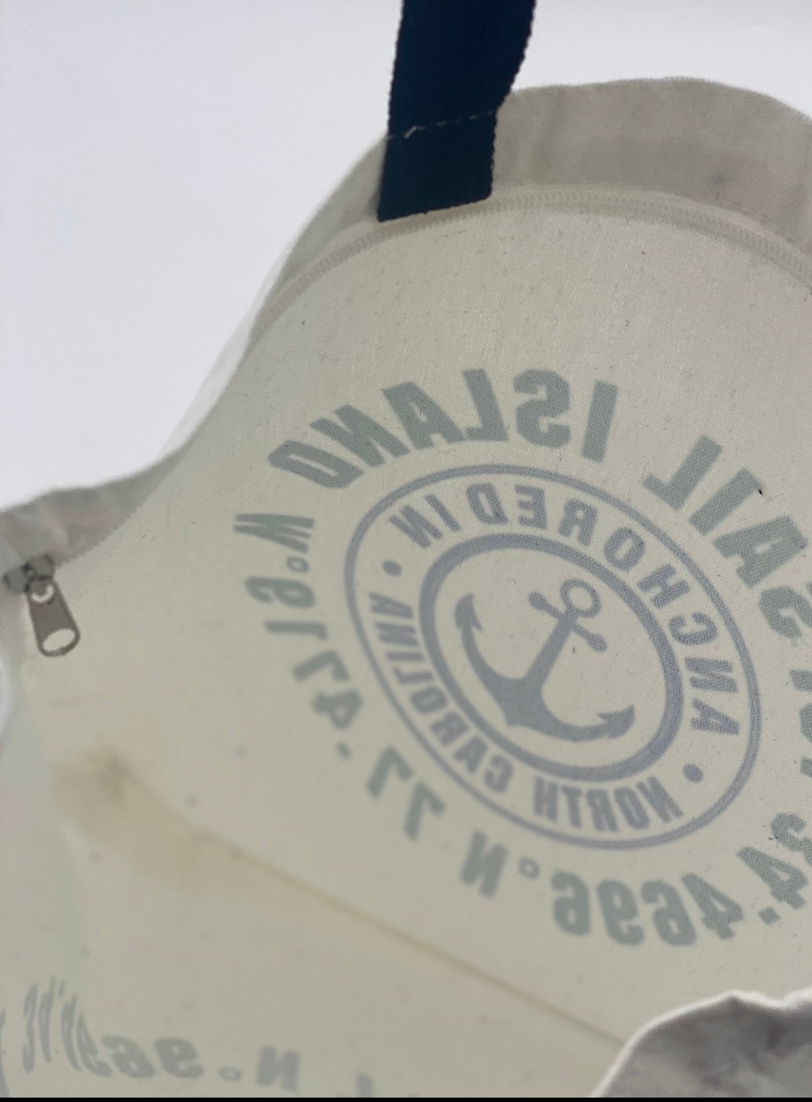 White tote bag with black handles, featuring a circular design with text reading 'TOPSAIL ISLAND,' 'ANCHORED IN,' and 'NORTH CAROLINA,' along with an anchor symbol and geographic coordinates.