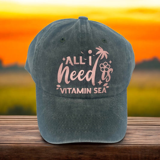 Green cap with 'All I Need is Vitamin Sea' text against a sunset background