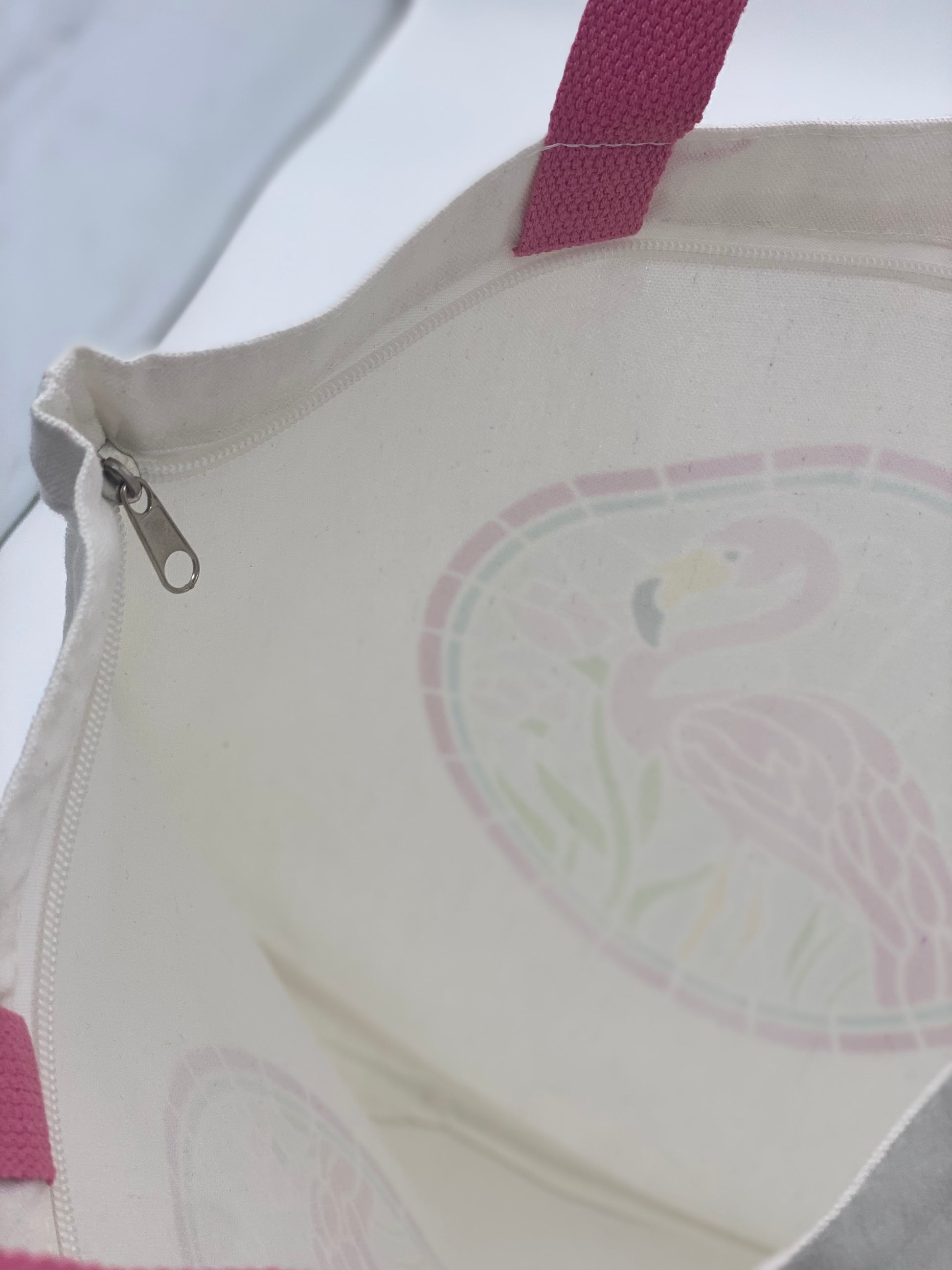 Close-up of inside white canvas bag with flamingo design featuring pink handles.