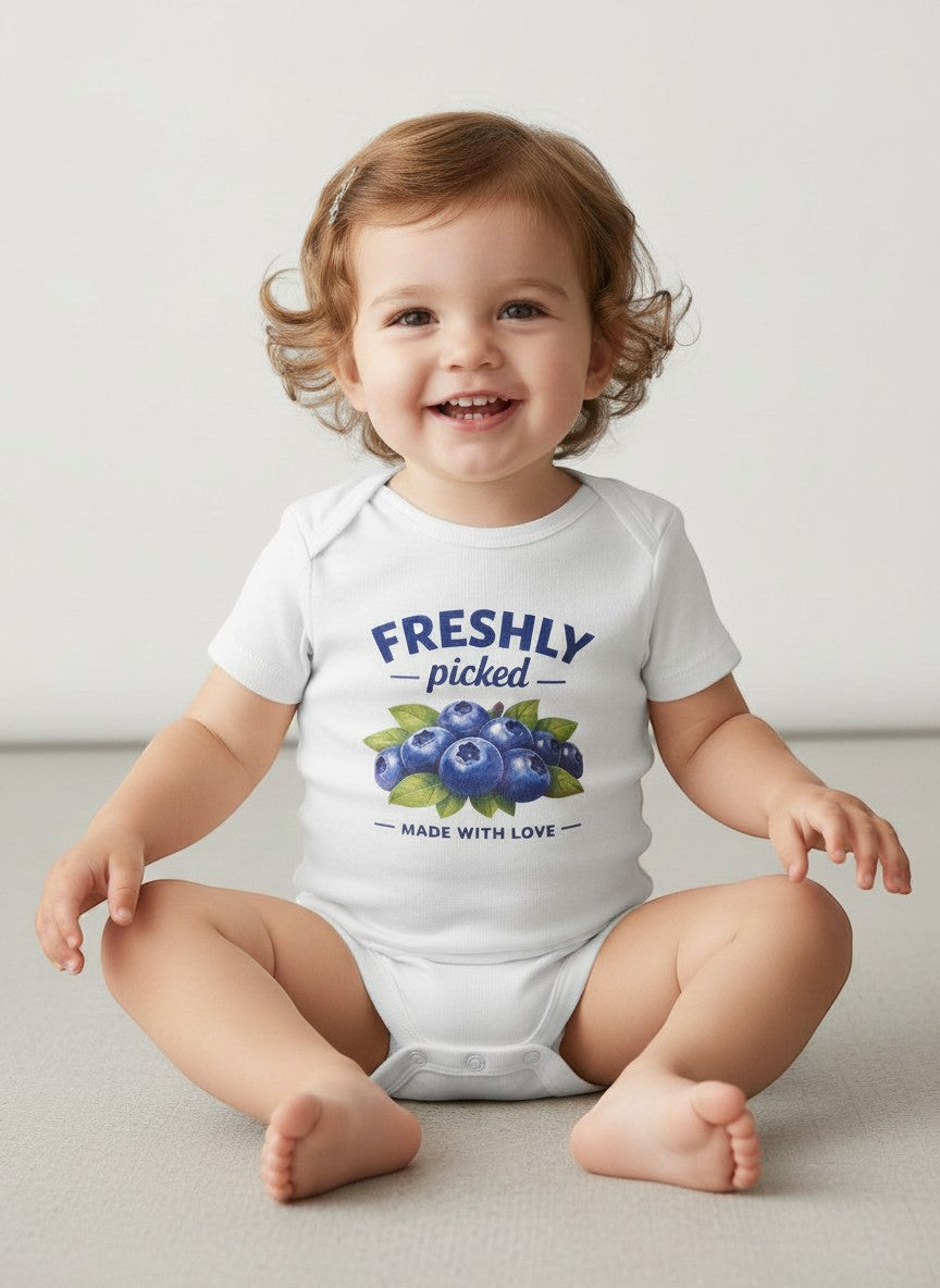 A smiling baby wearing a white Seaside Custom Apparel & Gifts cotton onesie with a Freshly Picked Made with Love print.