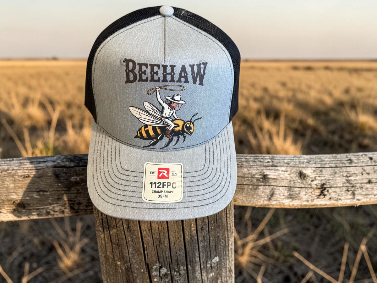 Seaside Custom Apparel & Gifts grey and black Richardson trucker hat featuring a Beehaw graphic on a wooden fence.