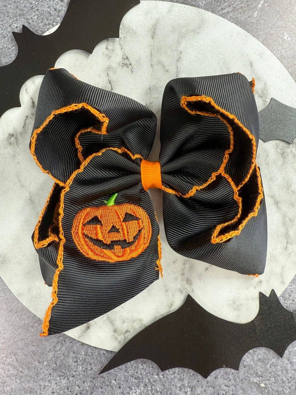 Seaside Custom Apparel & Gifts black hair bow with orange jack-o-lantern embroidery and decorative moonstitch edges.