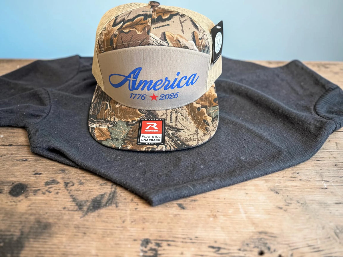 Seaside Custom Apparel & Gifts patriotic camo trucker hat with America embroidery and mesh back on a wooden table
