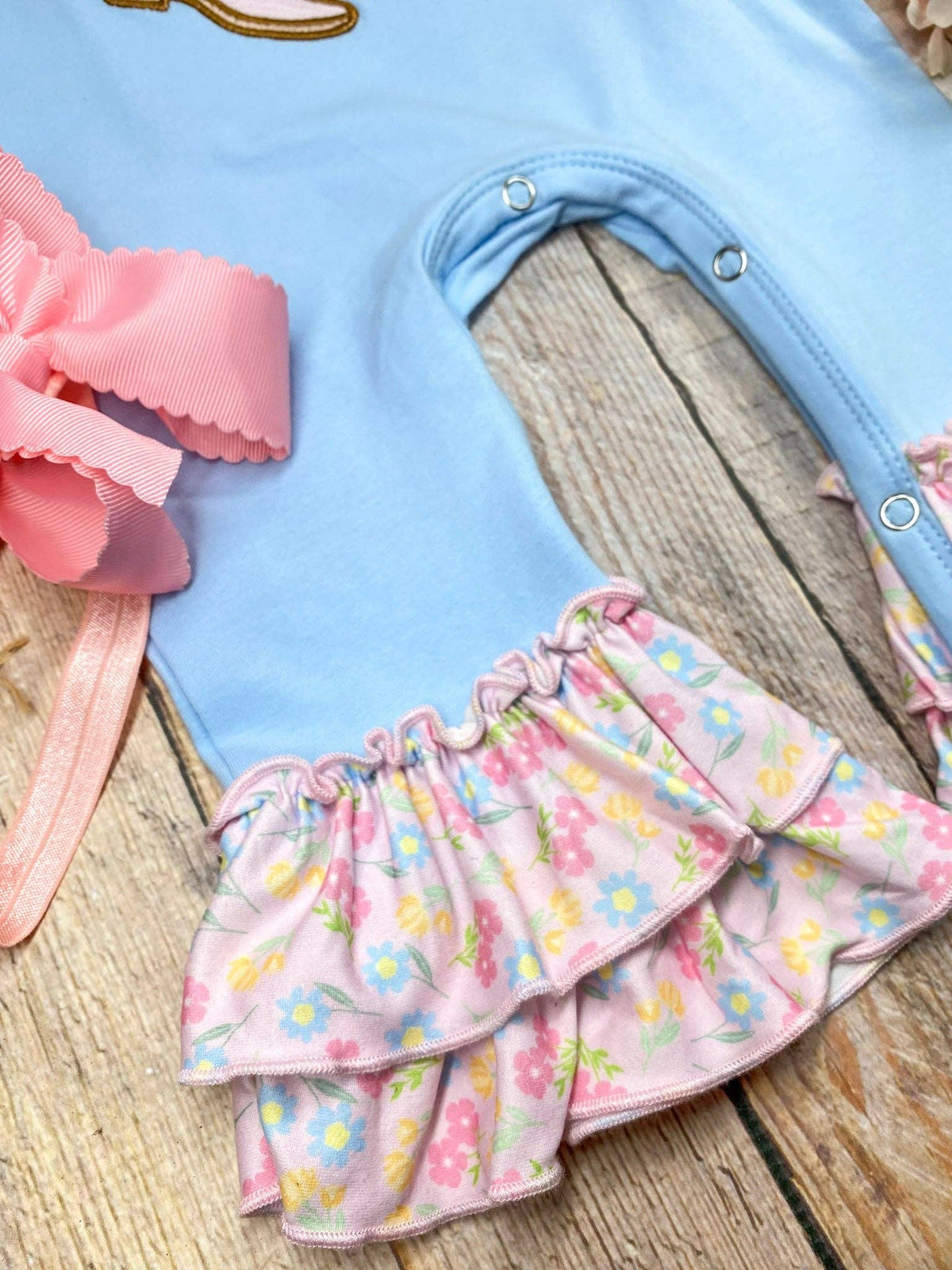 Seaside Custom Apparel & Gifts infant romper in blue with floral ruffle leg hems and a pink bow detail