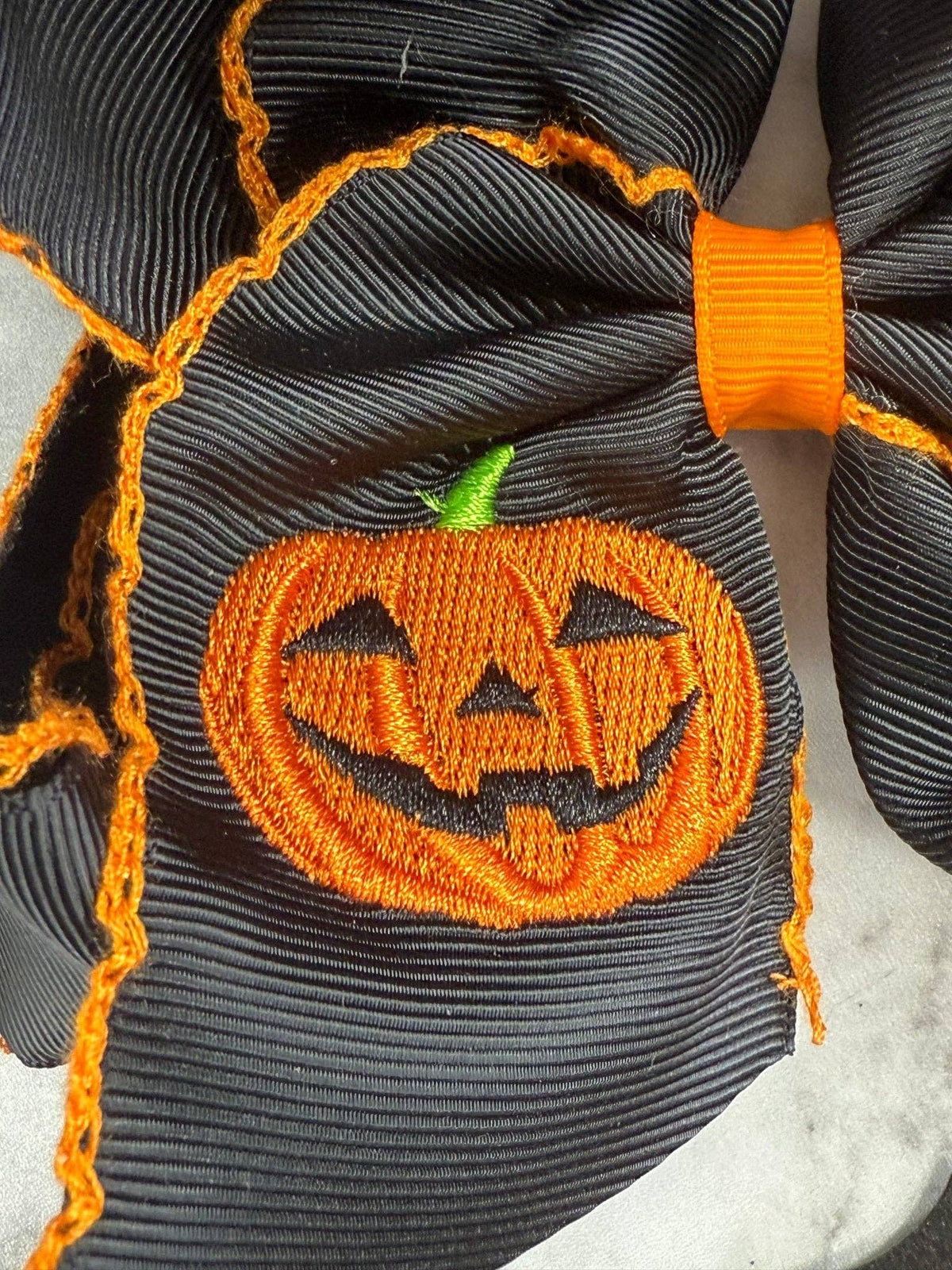 Seaside Custom Apparel & Gifts black hair bow with orange jack-o-lantern embroidery and decorative moonstitch edges.