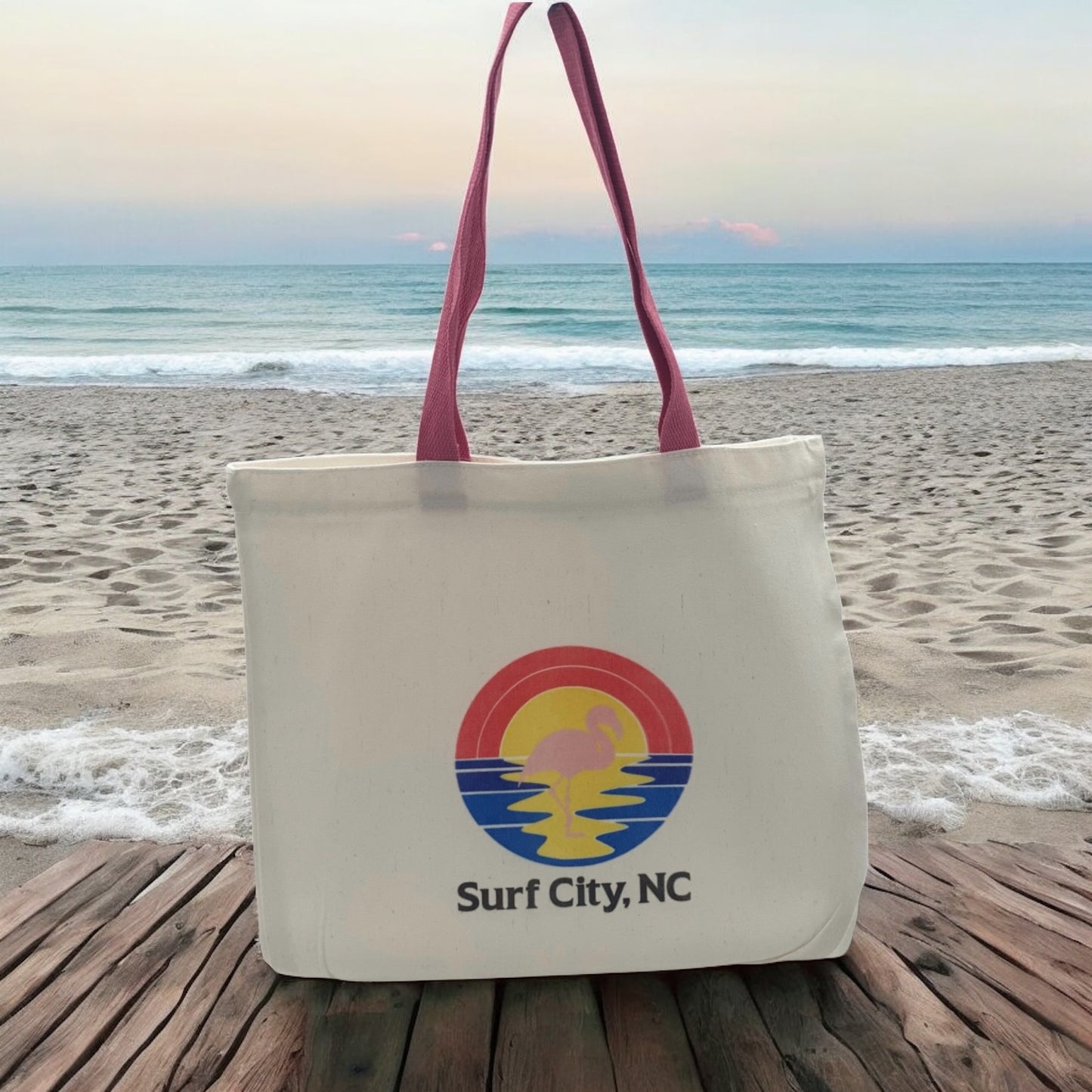 White tote bag with 'Surf City, NC' logo featuring pink flamingo standing in beach sunset.