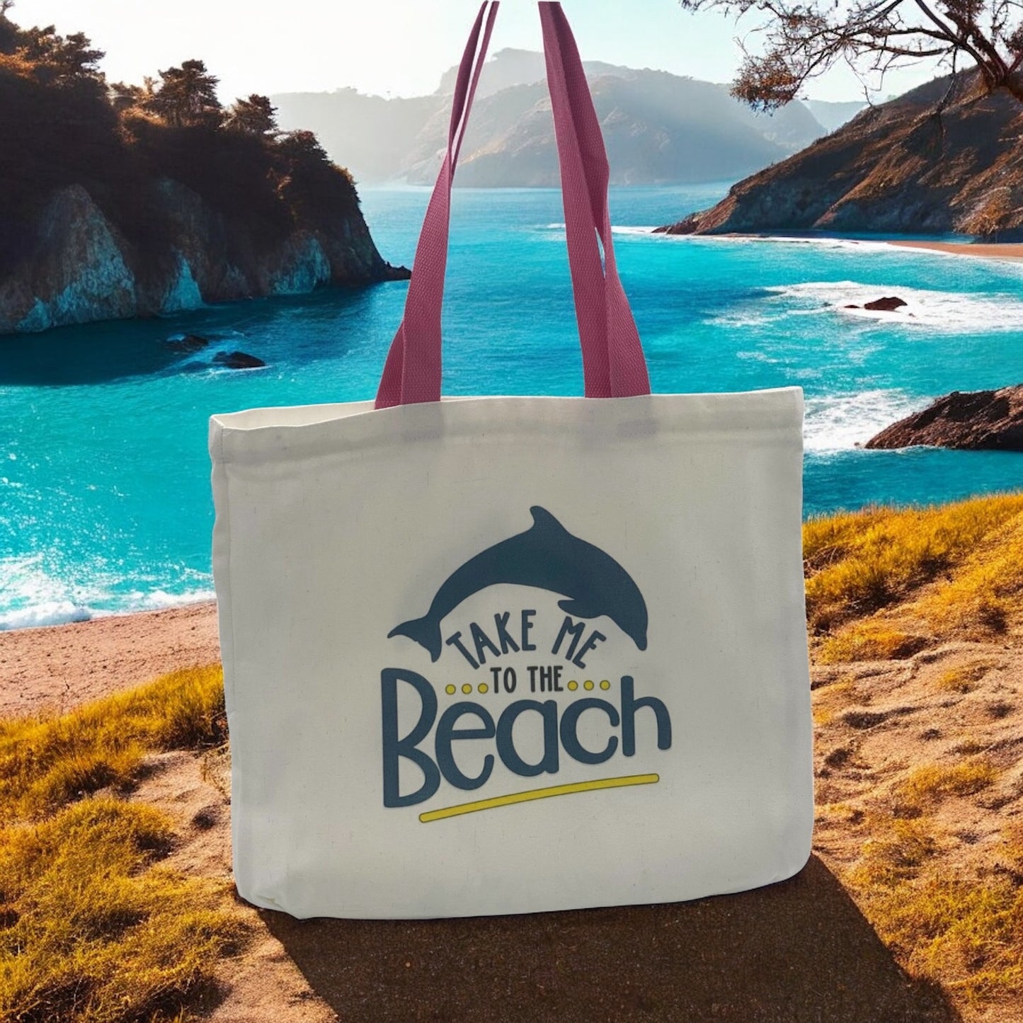 White Tote bag with pink handles featuring 'Take me to the Beach' text and dolphin graphic in front of a beach scene.