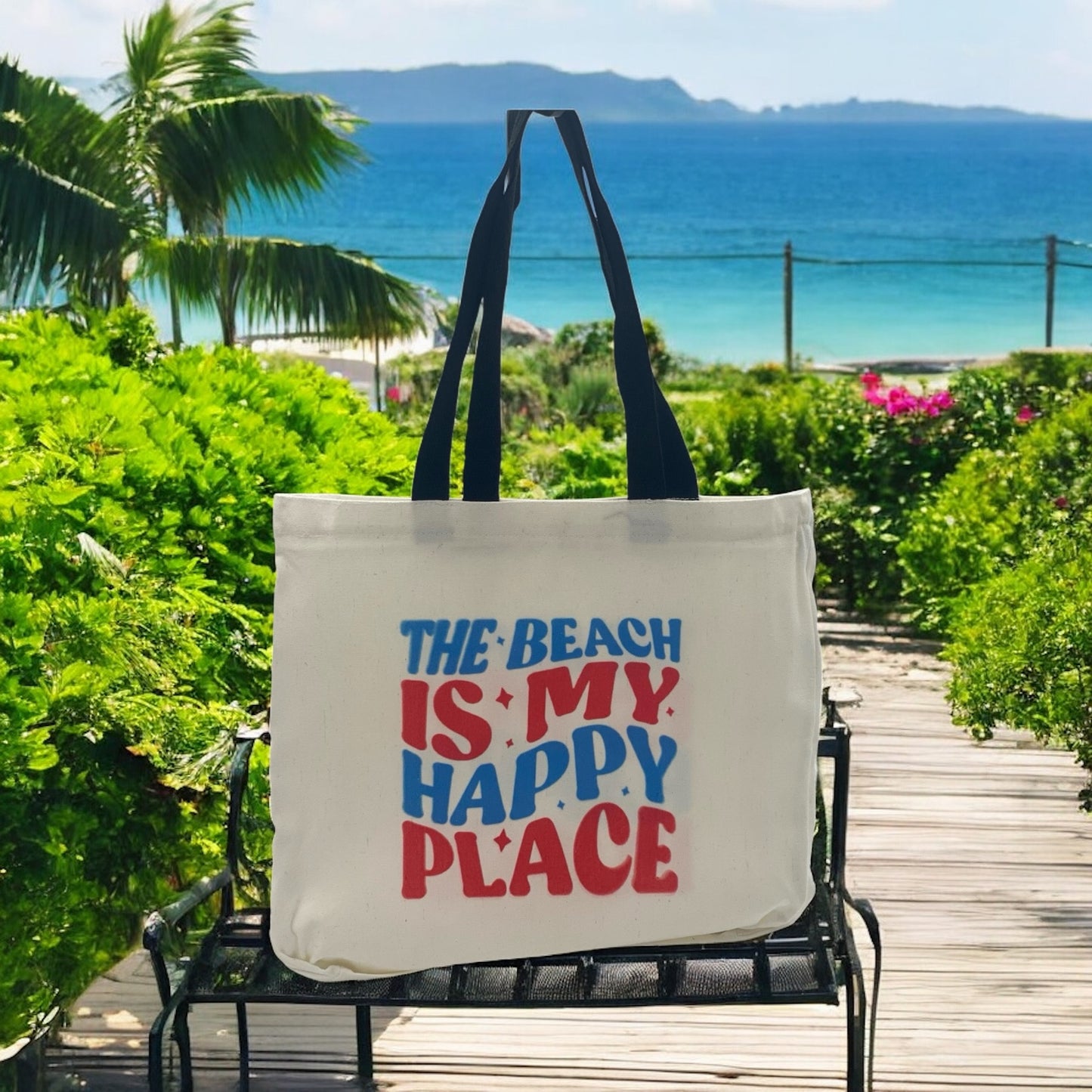 Tote bag with 'The Beach is My Happy Place' text on a chair by a scenic beach.